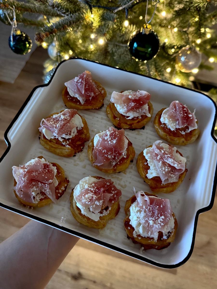 Tartinki z serkiem i szynką parmeńską na białym półmisku, w tle rozświetlona choinka