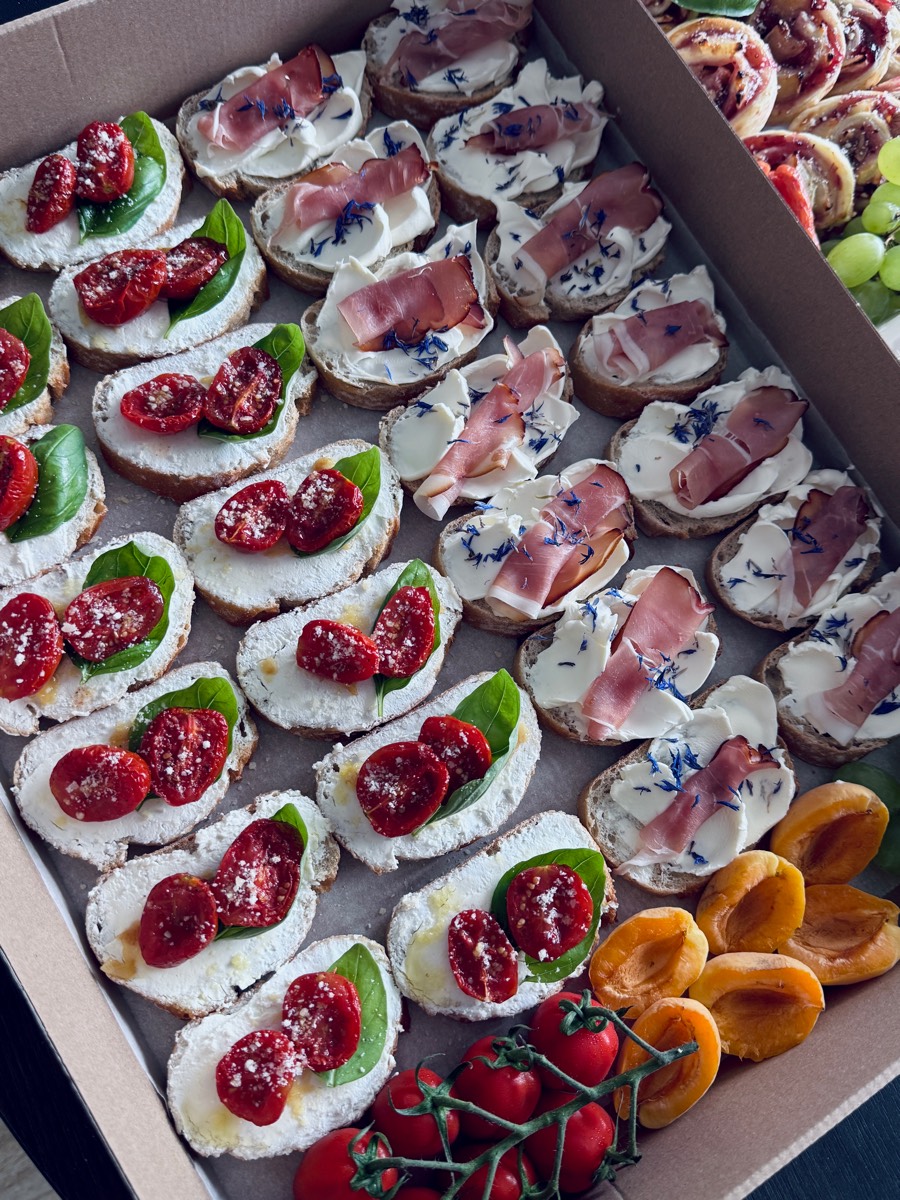 Box tartinek: serek z suszonym pomidorem i bazylią oraz serek z szynką i chabrami, obok morele i pomidorki na gałązce
