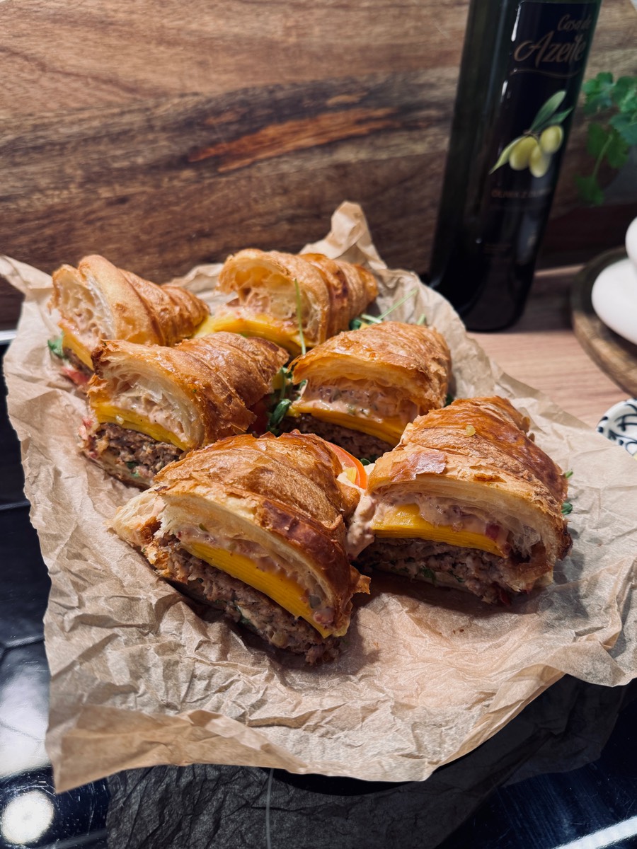Mini croissanty przekrojone na pół, z mięsnym nadzieniem i cheddarem, ułożone na papierze do pieczenia